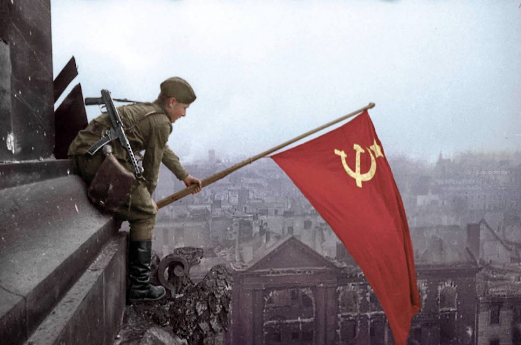 Żołnierz Armii Czerwonej zawiesza czerwony sztandar na gmachu Reichstagu, w tle ruiny pokonanego Berlina